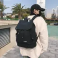 Black water-repellent large capacity school backpack with flap cover shown on a model outdoors - Black