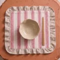 Pink and white striped linen ruffled placemat shown with ceramic bowl and wooden chopsticks - 42x42cm / Ruffle Trim Triple Stripe Linen Style / 1 Piece / Red