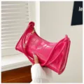 Detailed view of a stylish bright pink croc-embossed underarm bag held by hand - Rose Red