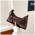 Detail view of a shiny dark burgundy crocodile-embossed underarm baguette bag for women - Brown