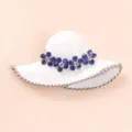 Detailed close-up of a white enamel hat brooch with sparkling blue rhinestones. - White