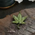 Macro view of vintage green maple leaf brooch with detailed enamel texture on wood - Maple Leaf