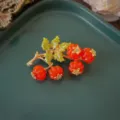 Dettaglio di una spilla barocca vintage con bacche di smalto rosso e foglie dorate. - Stile Bacche Arancioni Vintage