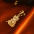 Elegant gold-toned violin brooch encrusted with sparkling crystals and a white pearl - White