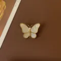 Close-up of a vintage butterfly brooch with gold frame and pearlescent wings on brown background - Baroque Pearl White Butterfly