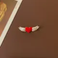 Macro detail of a vintage heart brooch with white enamel wings on brown background - Red Heart with Wings Style