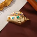 Primo piano di una spilla a conchiglia dorata vintage con vivaci cristalli colorati - Stile Conchiglia / Oro con Cristalli Multicolore