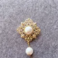 Detailed view of a vintage gold-tone brooch with elegant pearl accents on grey felt. - Vintage Hollow Pearl Style (B4) / Gold
