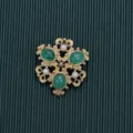 High-detail view of a vintage Baroque style brooch with green cabochons and pearls - Style 12