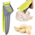 Detail shot of a green and grey manual garlic press crushing fresh garlic cloves into a bowl. - 果绿拼深灰
