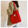 Detalle de un bolso de pana roja vibrante llevado sobre una chaqueta blazer de color caqui. - Rojo