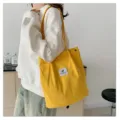 Vista lateral detallada de un bolso de pana amarillo con un parche de logo de hoja - Amarillo