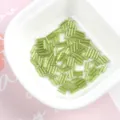 Detailed overhead view of 2x7mm silver-lined green glass bugle beads inside a white bowl - 20g/Pack / Light Green