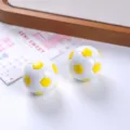 Close-up of small white and yellow resin soccer ball figurines featuring a glossy finish. - Yellow