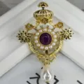 Primer plano detallado de un broche de corona barroca dorada con gema púrpura y perla - Estilo Corona Barroca / Dorado con piedra púrpura