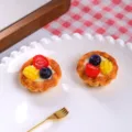 Detaillierte Makroansicht von zwei realistischen Obsttörtchen aus Harz auf einem weißen Teller. - Mango Erdbeere Eiertarte