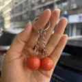 Detailopname van een 2 cm oranje cricketbal-stijl dubbele sleutelhanger in de hand gehouden - Rode Cricketbal Stijl / 2cm