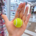Primer plano de un mini llavero de pelota de tenis en una mano abierta. - Estilo Tenis / 3.2cm / Verde