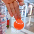 Detalle de un llavero de pelota de tenis naranja con anillo y cadena de metal plateado. - Estilo Tenis / 3.2cm / Naranja