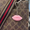 Detail shot of a glossy pink resin lip keychain hanging on a stylish brown patterned bag - Keychain / Pink