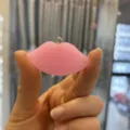 Macro detail view of a glossy pink resin lip-shaped pendant jewelry accessory held by hand - Pendant/Finding / Pink