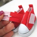 Nahaufnahme eines roten Miniatur-Puppenschuhs aus Stoff mit weißem Klettverschluss. - 5x2.5x3cm / Rot