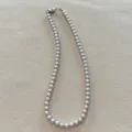 Detailansicht einer eleganten grauen Kunstperlenkette auf neutralem strukturiertem Grund - 6mm / Premium Grau