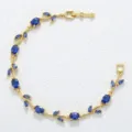 Elegante gouden wijnstok armband met blauwe kristallen op een witte achtergrond - Goud Blauwe Steen