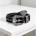 Close-up of black glitter western belt with silver carved floral buckle and star studs detail. - Black