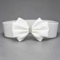 Close-up detail of white elastic waist belt featuring a rhinestone bow decoration. - White