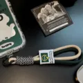 Λεπτομέρεια πράσινου και μπεζ πλεκτού ιμάντα καρπού κινητού με λευκή υφασμάτινη ετικέτα - Πράσινο και κίτρινο λουράκι με ετικέτα / Διαφανής Κάρτα