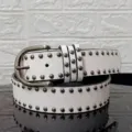 Close-up detail of white vintage punk belt with round metal rivets and silver buckle - White