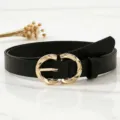 Detailed close-up shot of a stylish women's black leather belt with a shiny gold metal buckle. - Black