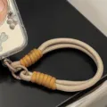Gros plan détaillé d'une dragonne de téléphone tressée bicolore avec anneau de fixation - Sangle Jaune et Café / Carte Transparente