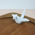 Detailed macro view of a white ceramic style origami crane chopstick rest on wood - White