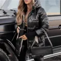 Detail shot of a shiny black hooded puffer jacket with stylish metallic hardware. - S / Tops / Black
