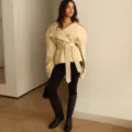 Detailed shot of a stylish beige belted coat worn by a model in a modern indoor setting. - XS / Tops / Light Yellow