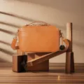 Vintage tan leather camera bag displayed on artistic wooden blocks with soft shadows. - Earthy Yellow