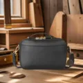 Vintage black leather camera bag with gold hardware in a rustic workshop setting - Black