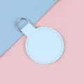 Porte-clés rond en cuir bleu ciel avec anneau argenté sur fond pastel bicolore - Bleu Glacé