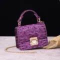 Primer plano de bolso de lujo en cuero violeta con grabado de cocodrilo y cierre dorado. - Púrpura Oscuro (PG877 Púrpura Oscuro)