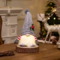 Warm glowing Christmas gnome ornament with gray knitted hat on rustic wooden base - Grey