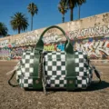 Stylish green and white checkerboard travel bag featured against an urban graffiti wall. - Green