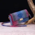 Detalle de un vibrante bolso bandolera de cuero con relieve de cocodrilo en lila y azul. - Púrpura y Azul