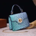 Detail of a teal crocodile-embossed retro handbag with gold-tone metal lock and chain strap. - Blue Green Gradient