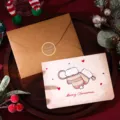 Vista detallada de tarjeta navideña de mitones y sobre kraft sobre bandeja de madera - Manoplas de Navidad