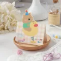 Vouwbare cartoon wenskaart met een schattige beer op een gele eend voor kinderen - Teddybeer
