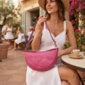 Modelo con un bolso bandolera rosa vintage en forma de medialuna en un café exterior - Rosa rojo