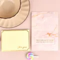 Detalle de tarjeta de felicitación bronceada con patrón de mármol rosa y frases románticas. - Nubes En El Cielo, Tú En Mi Corazón / Sobre Estampado en Oro + Bolsa OPP