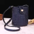 Vista detallada de un bolso bandolera azul con relieve de cocodrilo y cierre dorado. - Azul